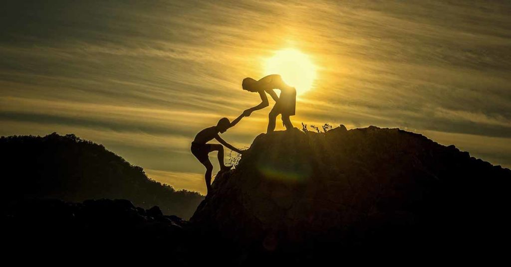 Picture of sunset behind mountains with two young man climbing.