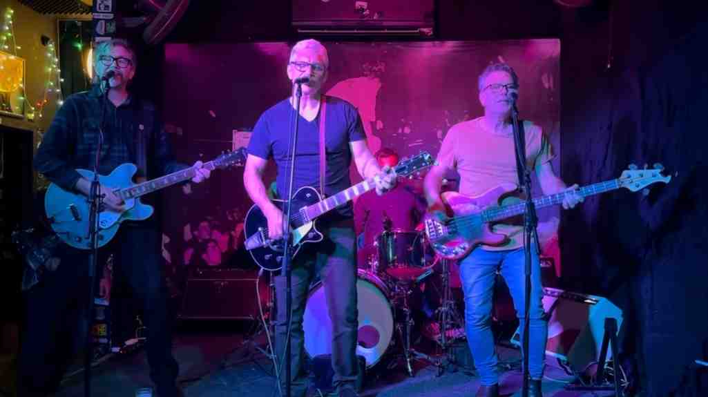 The Silversteins performing on stage with singer, two guitarists, bass player and drummer, all lit by soft pink stage lighting.