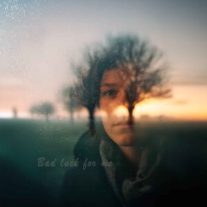 Sunset field with blurred oak trees and a softly blurred woman emerging from the background, featuring the handwritten title Bad Luck for Me.