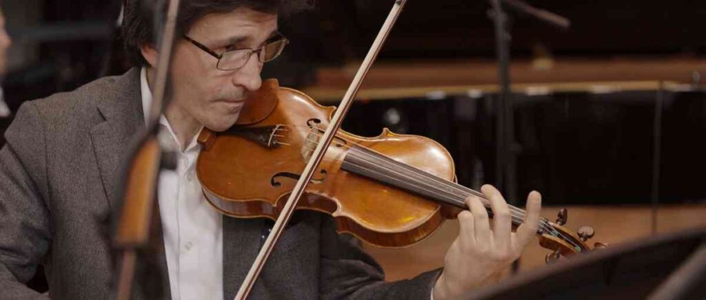 Close up of a violinist during a recording session, showing the violin body, bow in motion, and part of the player’s focused face.